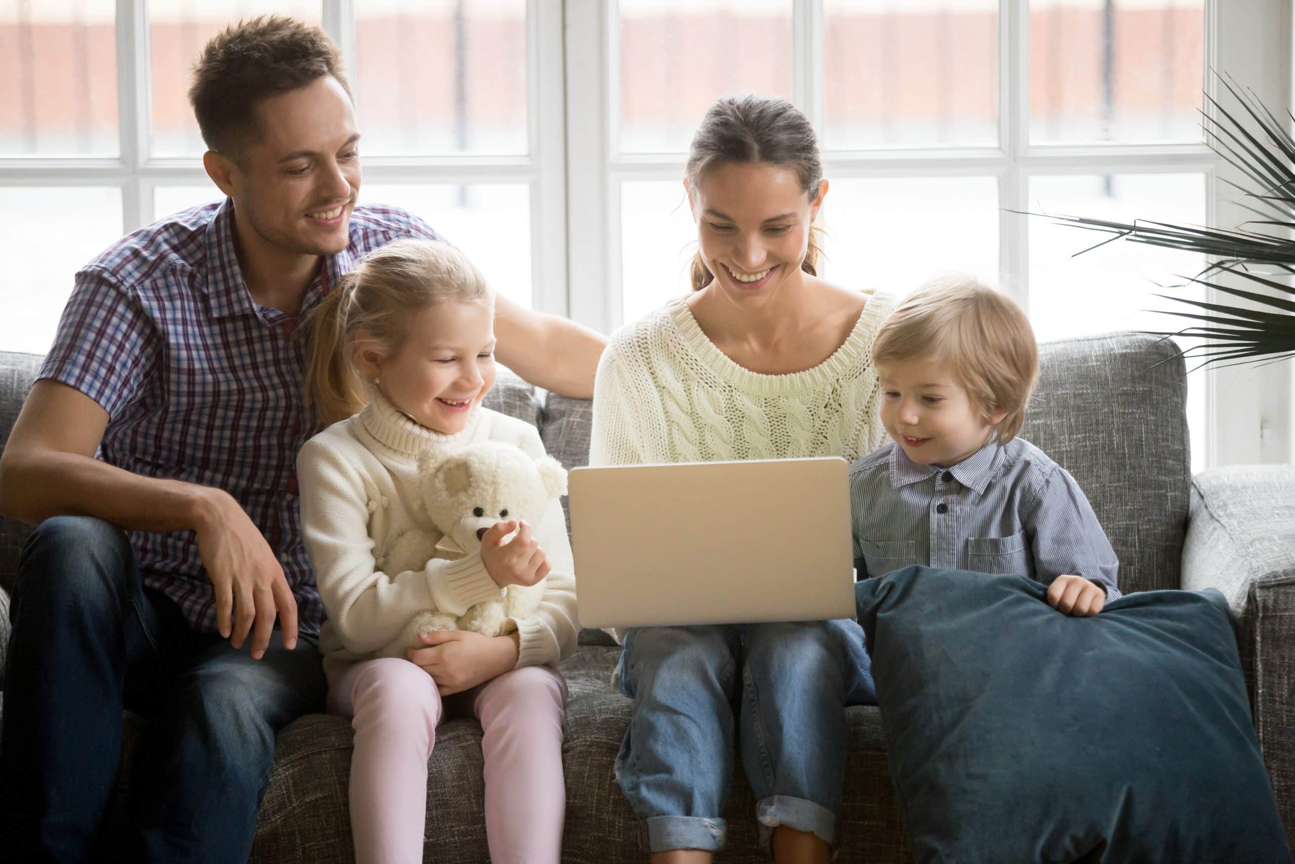 a family sitting on a couch looking at a laptop